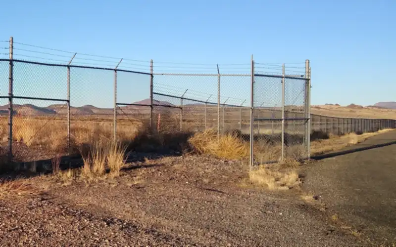 Chain link security fence topped with barbed wire, with a tall gate, around a rural airfield in dry grassland